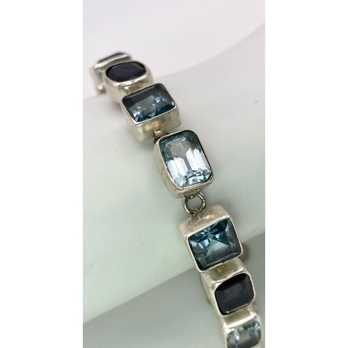 935 - A Blue Topaz and Iolite Tennis Bracelet set in 925 Sterling Silver. 51ctw. W-25.5g. 20cm length. Ref... 