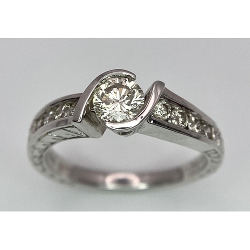 19 - An 18K White Gold Diamond Crossover Ring. 0.50ct tinted brilliant round cut diamond with eight round... 