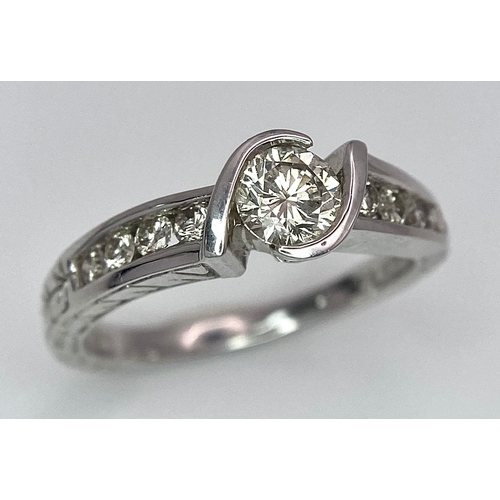 19 - An 18K White Gold Diamond Crossover Ring. 0.50ct tinted brilliant round cut diamond with eight round... 