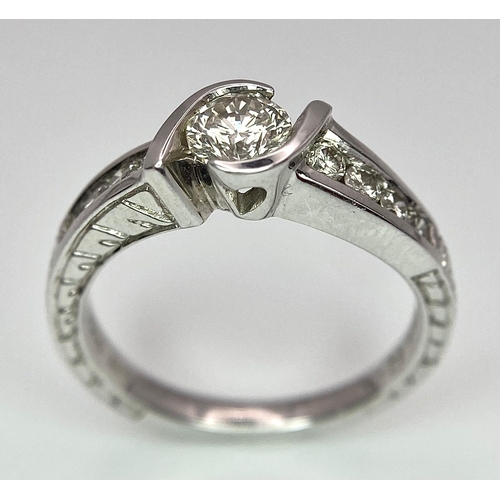 19 - An 18K White Gold Diamond Crossover Ring. 0.50ct tinted brilliant round cut diamond with eight round... 