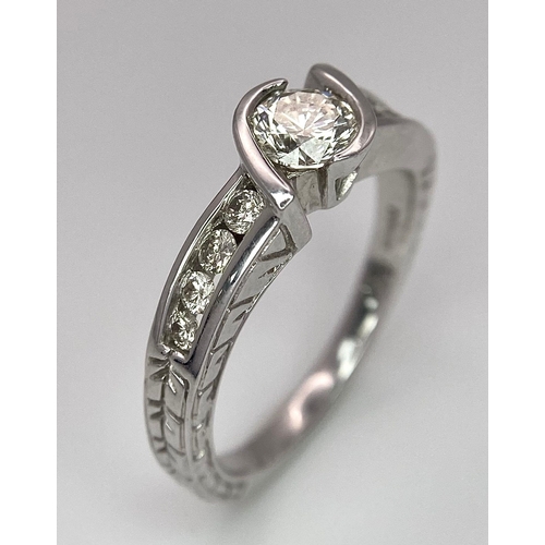 19 - An 18K White Gold Diamond Crossover Ring. 0.50ct tinted brilliant round cut diamond with eight round... 