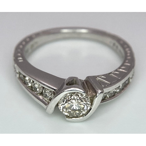 19 - An 18K White Gold Diamond Crossover Ring. 0.50ct tinted brilliant round cut diamond with eight round... 