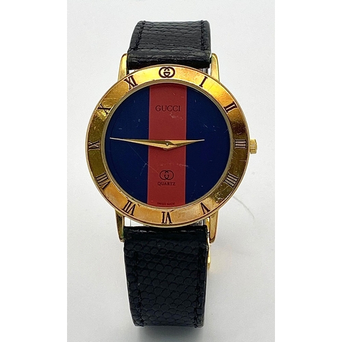 268 - An iconic GUCCI watch with original lizard skin strap. Case: 33 mm, red/blue dial with gold coloured... 