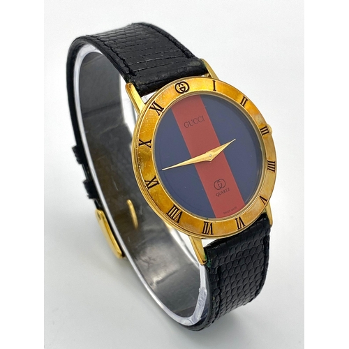 268 - An iconic GUCCI watch with original lizard skin strap. Case: 33 mm, red/blue dial with gold coloured... 