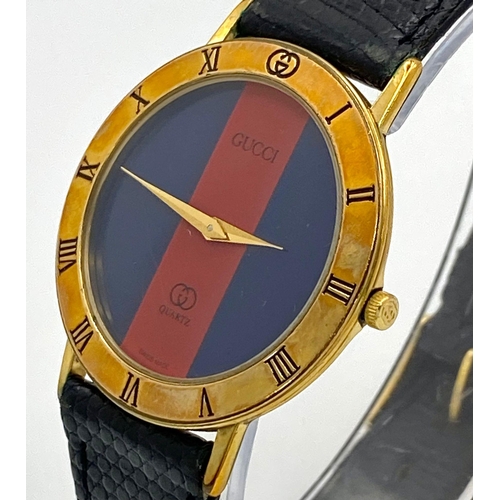 268 - An iconic GUCCI watch with original lizard skin strap. Case: 33 mm, red/blue dial with gold coloured... 