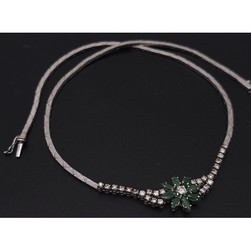 144 - An 18K White Gold Diamond and Emerald Necklace. A scale pattern necklace that leads to an emerald fl... 