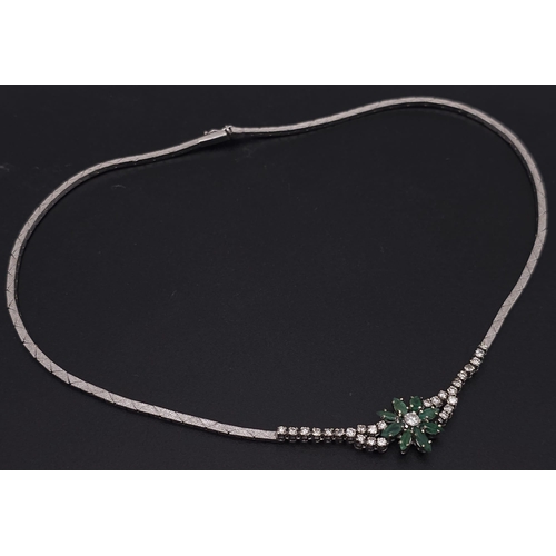 144 - An 18K White Gold Diamond and Emerald Necklace. A scale pattern necklace that leads to an emerald fl... 