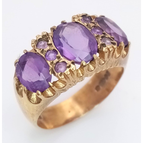 779 - A REGAL LOOKING 9K GOLD RING WITH A TRILOGY OF LARGE AMETHYST STONE SURROUNDED BY 6 SMALL AMETHYST S... 