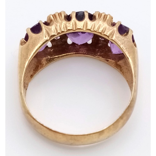 779 - A REGAL LOOKING 9K GOLD RING WITH A TRILOGY OF LARGE AMETHYST STONE SURROUNDED BY 6 SMALL AMETHYST S... 