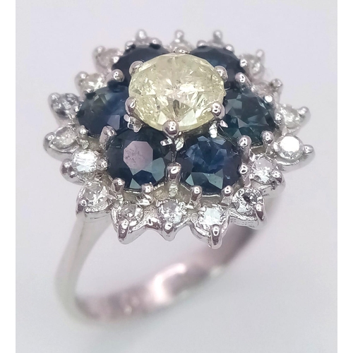 113 - An 18K White Gold Diamond and Sapphire Ring. Central tinted 1ct diamond with sapphire and white diam... 