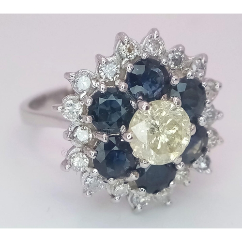 113 - An 18K White Gold Diamond and Sapphire Ring. Central tinted 1ct diamond with sapphire and white diam... 