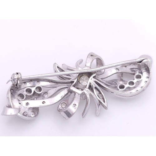 130 - A vintage, 9 K white white gold broch with an elaborate bow design adorned with two large round cut ... 