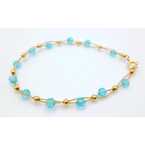 458 - An unusual 18 K yellow gold bracelet with two gold wires carrying alternating blue crystal faceted b... 