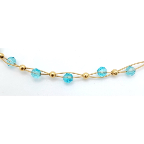 458 - An unusual 18 K yellow gold bracelet with two gold wires carrying alternating blue crystal faceted b... 