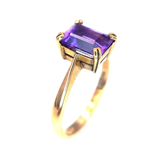 225 - A 9K GOLD RING WITH AN EMERALD CUT CENTRE AMETHYST .   2.8gms   size O