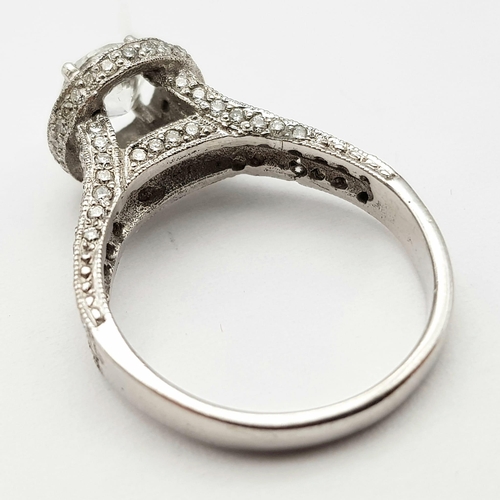 123 - An 18 K white gold ring with a brilliant cut diamond (1.01 carats) surrounded by diamonds on the top... 