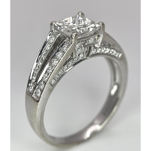24 - An 18K White Gold Diamond Ring. Central VS2 1ct Princess Cut Near White Diamond with Round Cut Diamo... 