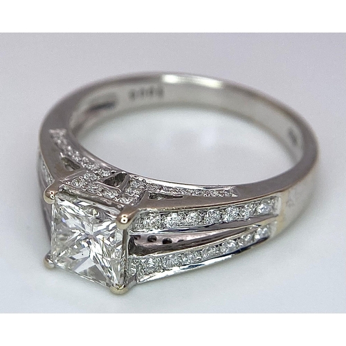 24 - An 18K White Gold Diamond Ring. Central VS2 1ct Princess Cut Near White Diamond with Round Cut Diamo... 