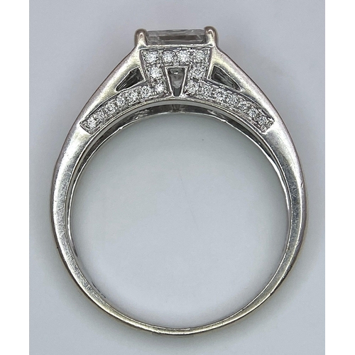 24 - An 18K White Gold Diamond Ring. Central VS2 1ct Princess Cut Near White Diamond with Round Cut Diamo... 