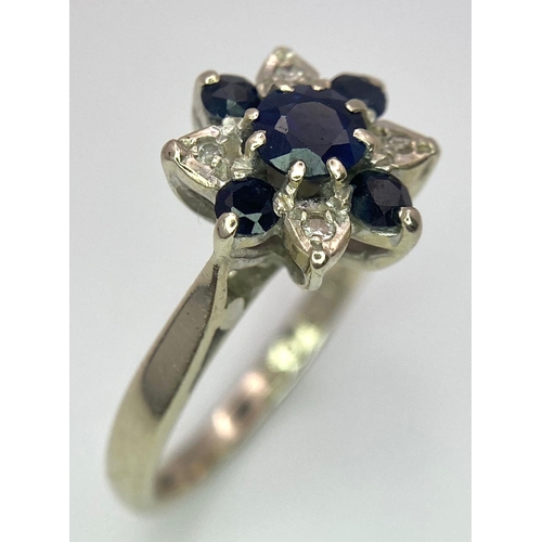 115 - An 18 K white gold ring with a cluster of diamonds and dark blue sapphires.  Size: M, weight: 4 g.