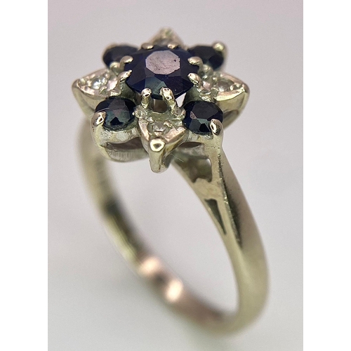 115 - An 18 K white gold ring with a cluster of diamonds and dark blue sapphires.  Size: M, weight: 4 g.
