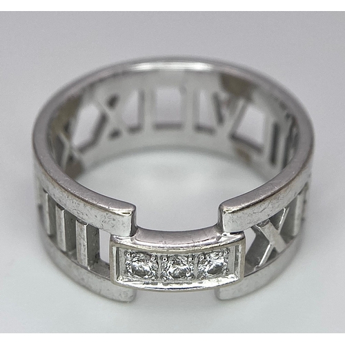 64 - An 18K White Gold Tiffany Atlas Diamond Ring. Pierced Roman numeral decoration. Tiffany mark. Size N... 