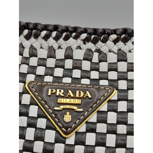 129 - A Prada Black and White 'Madras' Clutch Bag. Woven leather exterior with gold-toned hardware and zip... 