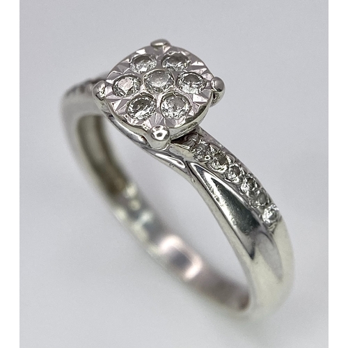 425 - A 9K White Gold Diamond Cluster Ring. Seven small diamonds on a circular base with diamonds on wings... 