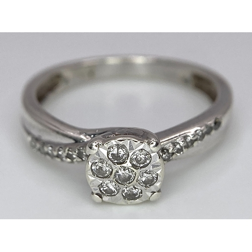 425 - A 9K White Gold Diamond Cluster Ring. Seven small diamonds on a circular base with diamonds on wings... 