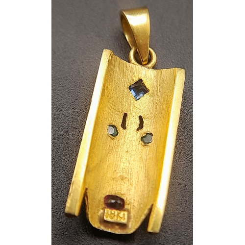 219 - A 18K (STAMPED AND TESTED AS) YELLOW GOLD CONGOLESE MASK PENDANT SET WITH SAPPHIRE, EMERALDS AND RUB... 