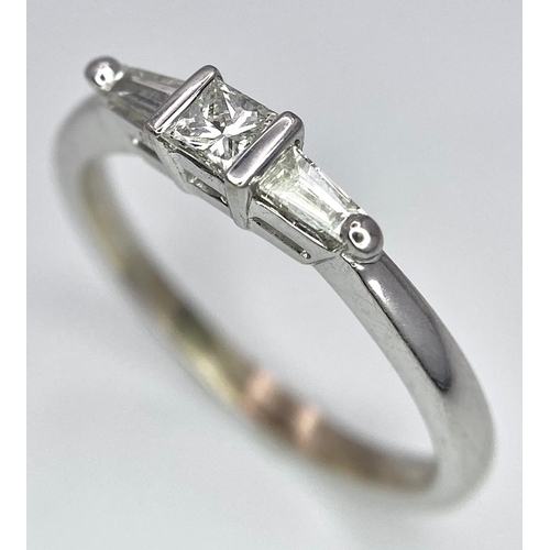 165 - AN 18K WHITE GOLD, DIAMOND 3 STONE RING - PRINCESS CUT CENTRE WITH A TAPPERED BAGUETTE DIAMOND EITHE... 