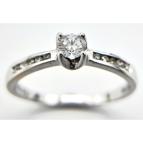 250 - AN 18K WHITE GOLD DIAMOND SOLITAIRE RING - WITH DIAMOND SHOULDERS. 0.25CT. 1.9G. SIZE L