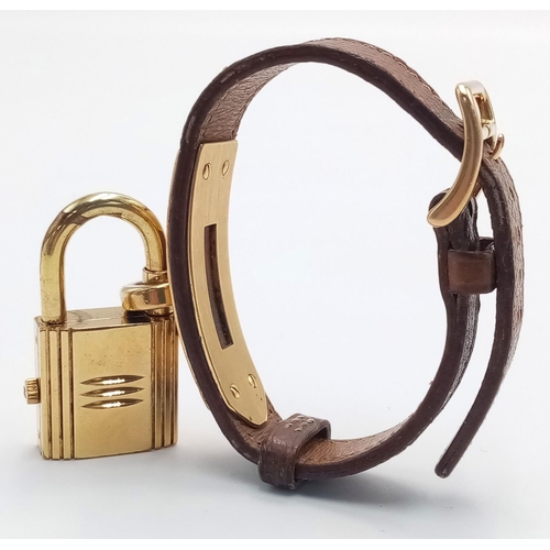 745 - A Hermes Kelly Watch. Brown leather strap. Gold plated padlock quartz watch. Needs a battery so as f... 