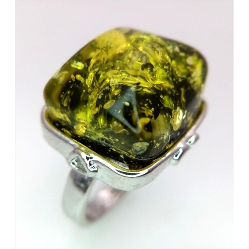 1446 - A white metal (untested) ring with a large yellow-green amber resin cabochon, size: T, weight: 12 g