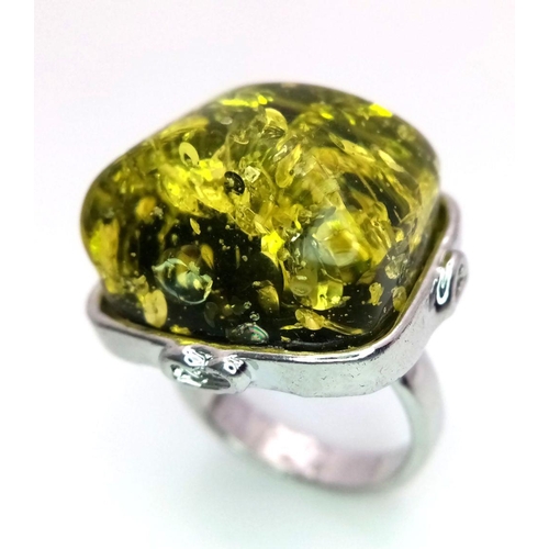 1446 - A white metal (untested) ring with a large yellow-green amber resin cabochon, size: T, weight: 12 g