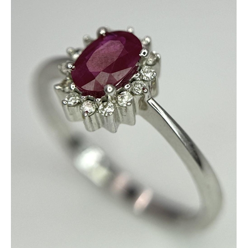 176 - An 18K White Gold Ruby and Diamond Ring. Central oval cut ruby with a diamond halo. Size N. 2.7g tot... 