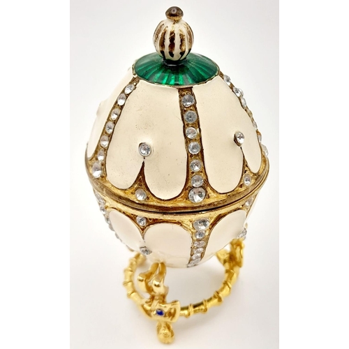 238 - A fabulous dress ring presented in a Faberge style egg resting on an elaborate base. Ring size: O