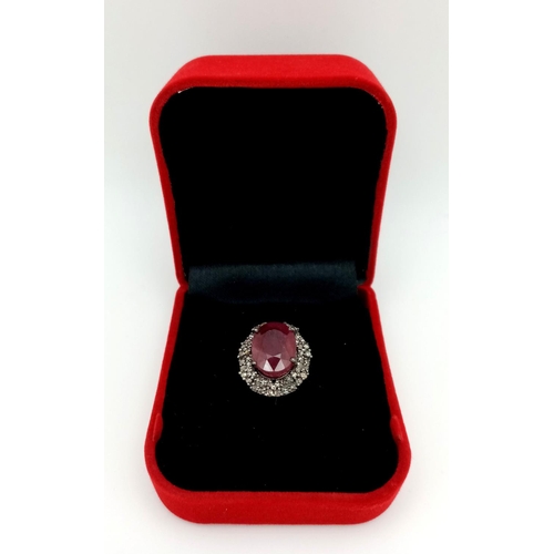 141 - A 6.35ct Oval Cut Ruby Ring with a 0.75ctw Diamond Surround - Set in 925 Silver. Size L. Comes with ... 