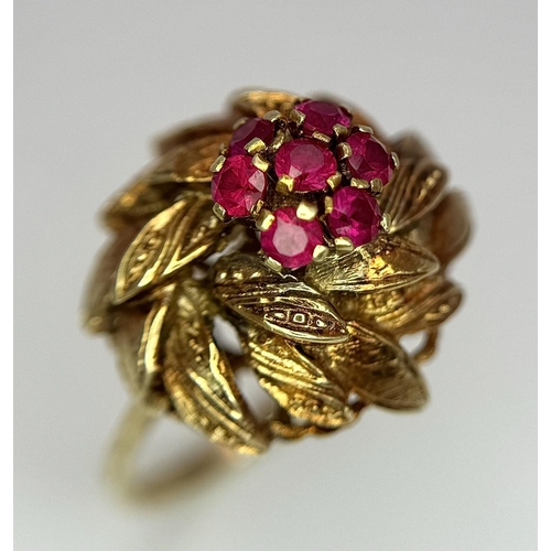 78 - An 18K Yellow Gold (tested) and Ruby Ring in Floral Form. Seven round cut rubies amidst leaves of 18... 