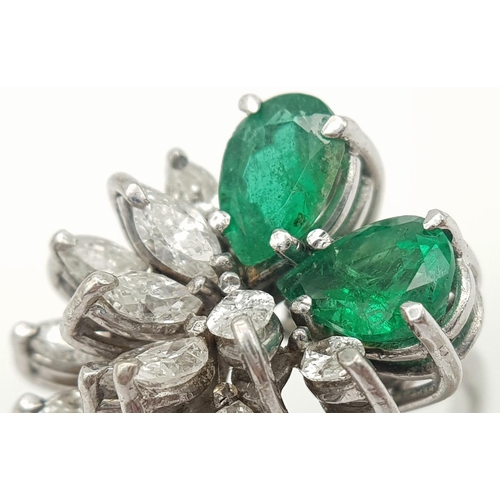 33 - An 18 K white gold ring with two rear cut emeralds counterbalanced  by a cluster of marquise cut dia... 