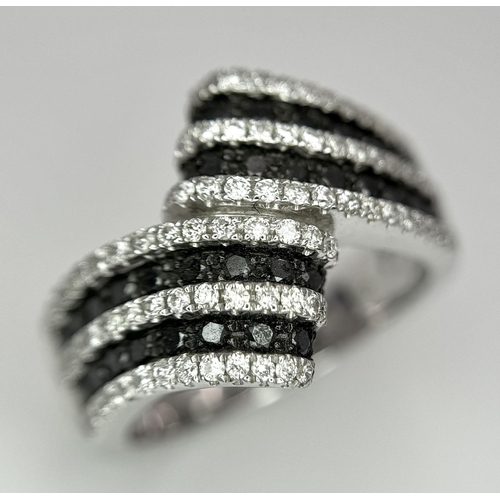 502 - A 14K WHITE GOLD WHITE & BLACK DIAMOND CROSSOVER RING. 1.25CT. 7.8G IN WEIGHT. SIZE N AND 1/2. Ref: ... 