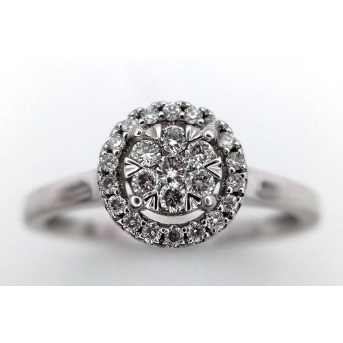 1072 - A 9K White Gold Diamond Cluster Ring. A circle of round cut diamonds with a halo of smaller round cu... 