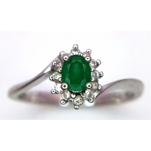 537 - A 18K WHITE GOLD 0.23CT DIAMOND & OVAL EMERALD CLUSTER TWIST RING. TOTAL WEIGHT 2.7G. SIZE M. REF ME... 