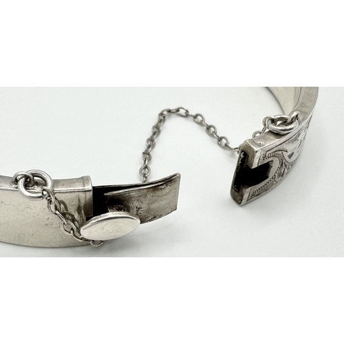 512 - A Sterling silver engraved bangle with bird motif and safety chain. 6.5cm wide, 16.1g in total weigh... 