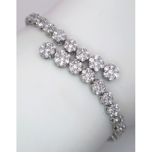 639 - An 18K White Gold and Diamond Bracelet. Graduating floral diamond cluster links that overlap. 1.5ctw... 