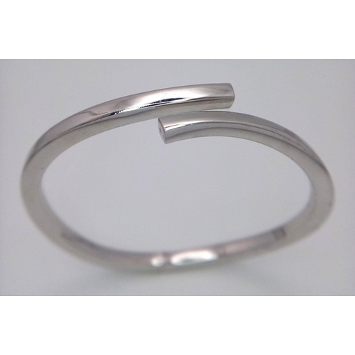 83 - A 9K WHITE GOLD CROSSOVER HINGED BANGLE - 12.7G. REF: JBA1