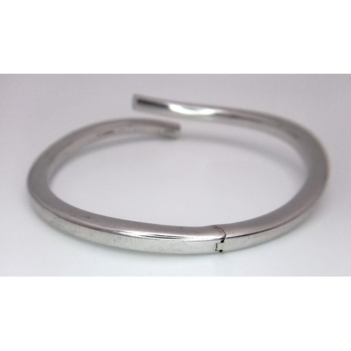 83 - A 9K WHITE GOLD CROSSOVER HINGED BANGLE - 12.7G. REF: JBA1