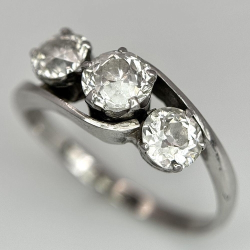 75 - An 18K White Gold Three Stone Diamond Crossover Ring. One central brilliant round cut diamond of 0.7... 