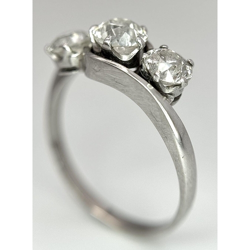 75 - An 18K White Gold Three Stone Diamond Crossover Ring. One central brilliant round cut diamond of 0.7... 