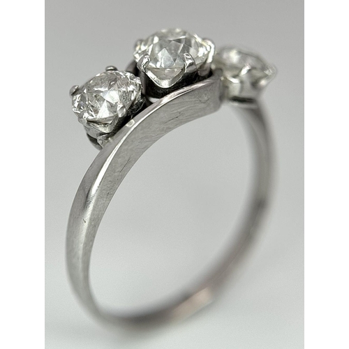 75 - An 18K White Gold Three Stone Diamond Crossover Ring. One central brilliant round cut diamond of 0.7... 